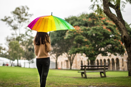 Frau mit regenbogenfarbigem Regenschirm in einem Park